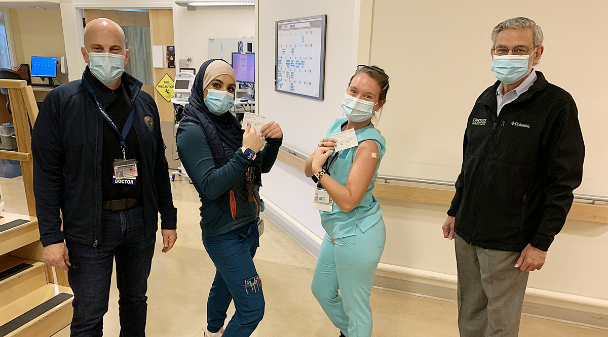Four hospital staff members wearing masks and standing in a hallway hospital.