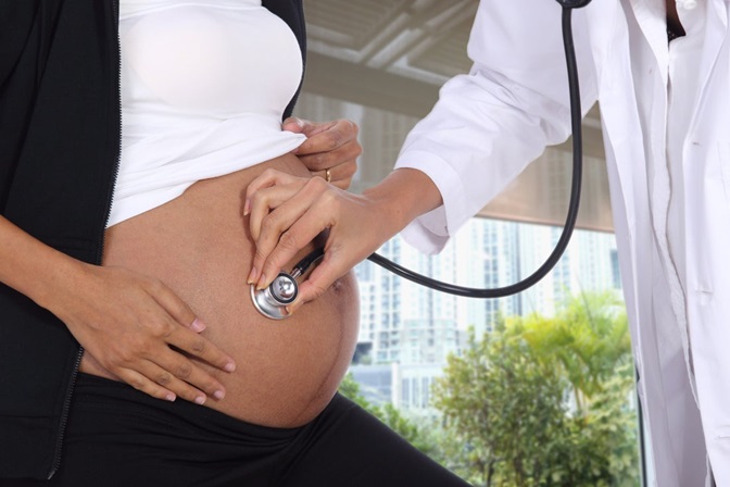 A pregnant patients exposes her bare belly while the physician puts a stethoscope against the belly. 