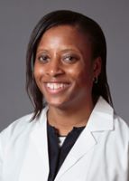 Shaundreal Jamison smiles for her headshot in a white coat on a gray background