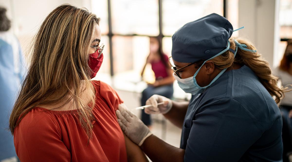 A female healthcare worker vaccinating a patient. Both are wearing masks.