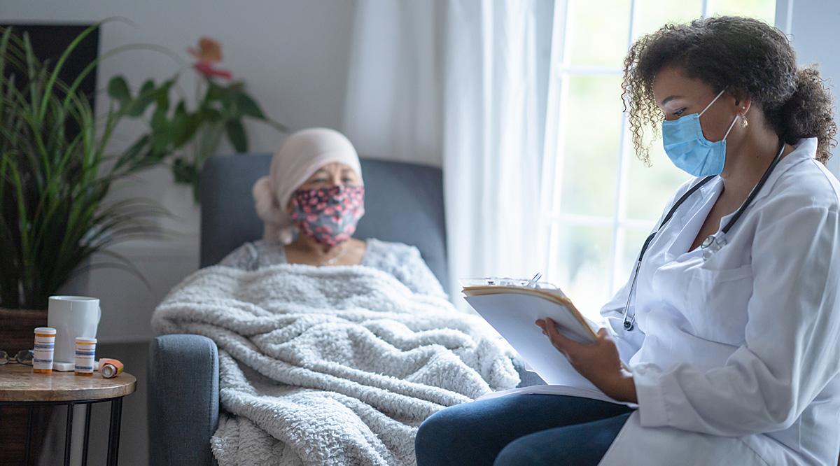 A female patient talking to a female doctor in a hospital room. Both are wearing masks.