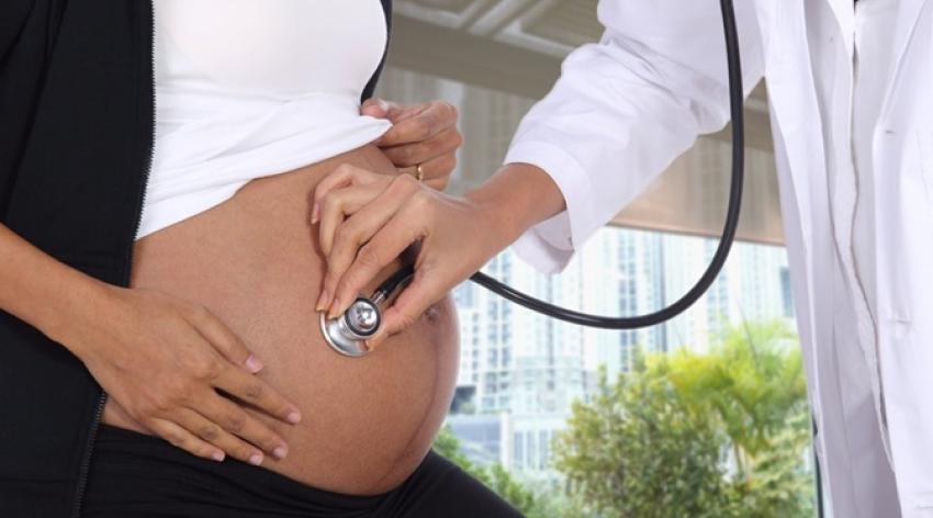 A pregnant patients exposes her bare belly while the physician puts a stethoscope against the belly. 